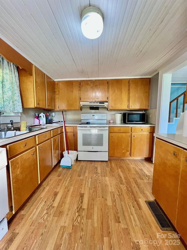 67 N Highland Ave, Granite Falls, NC 28630 - kitchen with white range with electric cooktop, stainless steel microwave, brown cabinetry, light wood-type flooring, and under cabinet range hood