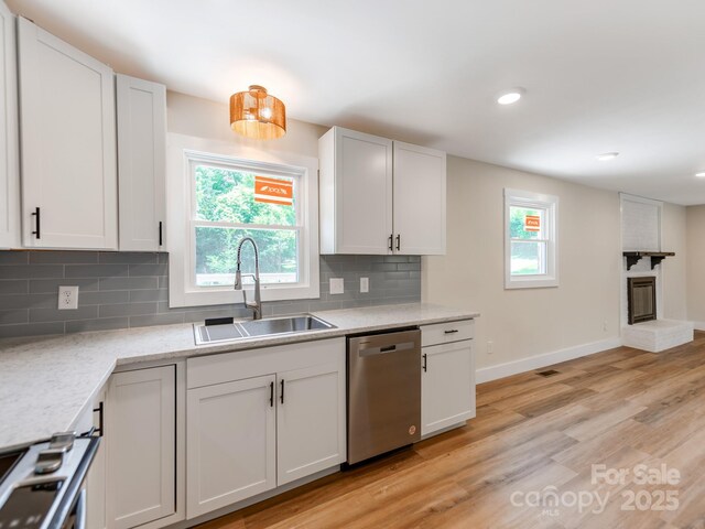 1606 N Rhyne St, Gastonia, NC 28054 - kitchen featuring dishwasher, decorative backsplash, light wood-style floors, a brick fireplace, and white cabinets