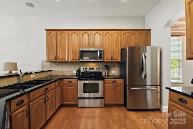 10818 Alvarado Way, Charlotte, NC 28277 - kitchen with stainless steel appliances, arched walkways, light wood-style floors, dark stone countertops, and tasteful backsplash