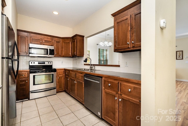 2773 Clover Rd NW, Concord, NC 28027 - kitchen featuring stainless steel appliances, decorative backsplash, a chandelier, light tile patterned floors, and brown cabinets