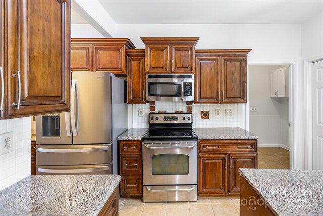 1581 Bluff Ct, Rock Hill, SC 29732 - kitchen with appliances with stainless steel finishes, light stone countertops, backsplash, light tile patterned floors, and brown cabinetry