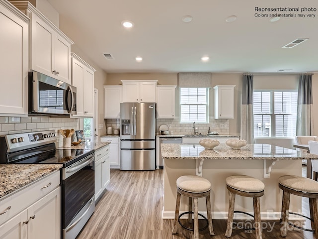 225 Runner Stone Ln, Fort Mill, SC 29715 - kitchen featuring stainless steel appliances, a kitchen bar, white cabinetry, backsplash, and light wood-style floors