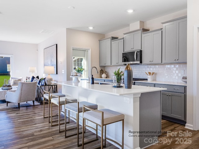 1016 Lookout Shoals Dr, Fort Mill, SC 29715 - kitchen featuring gray cabinetry, stainless steel microwave, a breakfast bar, backsplash, and dark wood-style flooring