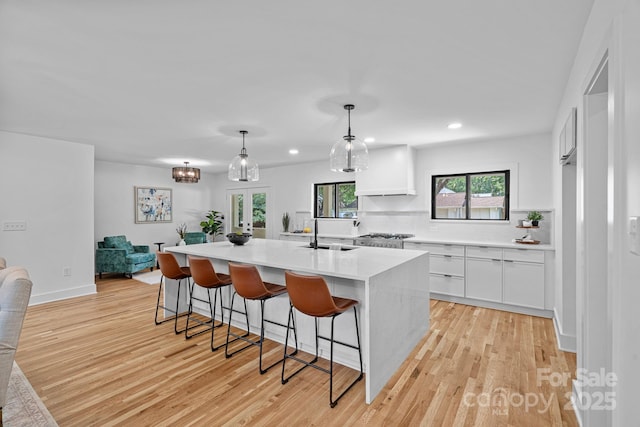 4209 Windwood Cir, Charlotte, NC 28226 - kitchen featuring light countertops, light wood finished floors, white cabinets, an island with sink, and a breakfast bar area
