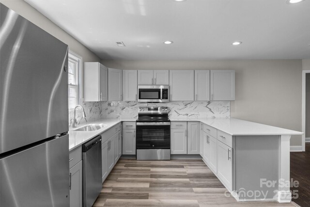 509 8th Avenue Ext, Cramerton, NC 28032 - kitchen featuring appliances with stainless steel finishes, a peninsula, recessed lighting, light wood-type flooring, and gray cabinetry