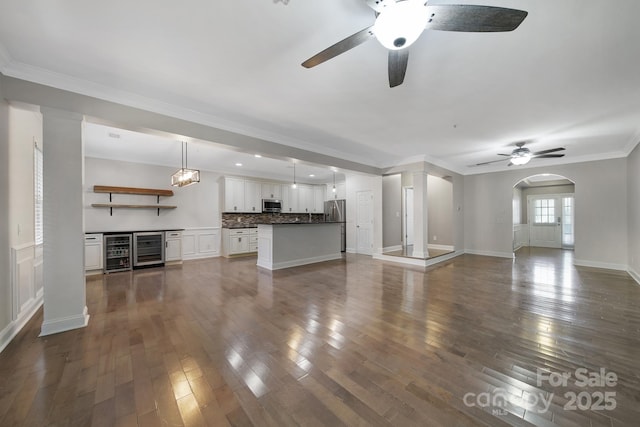 329 Wave Crest Dr, Tega Cay, SC 29708 - unfurnished living room with ceiling fan, wine cooler, dark wood-style floors, arched walkways, and ornamental molding
