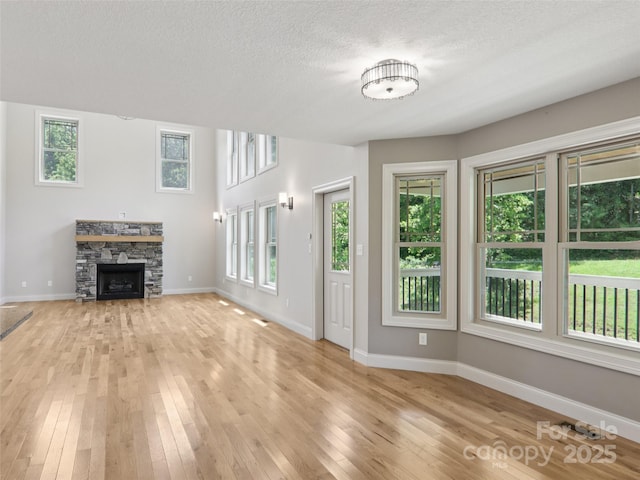 278 Ollie Weaver Rd, Weaverville, NC 28787 - unfurnished living room featuring light wood finished floors, plenty of natural light, a stone fireplace, and a textured ceiling