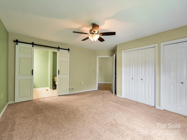 621 E Park Pl, Hendersonville, NC 28791 - unfurnished bedroom featuring a barn door, light colored carpet, multiple closets, ensuite bathroom, and ceiling fan