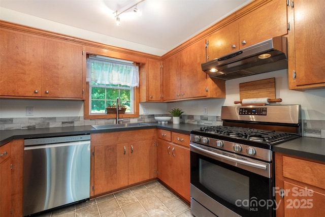 4919 Rehobeth Rd, Waxhaw, NC 28173 - kitchen featuring stainless steel appliances, under cabinet range hood, dark countertops, brown cabinets, and track lighting