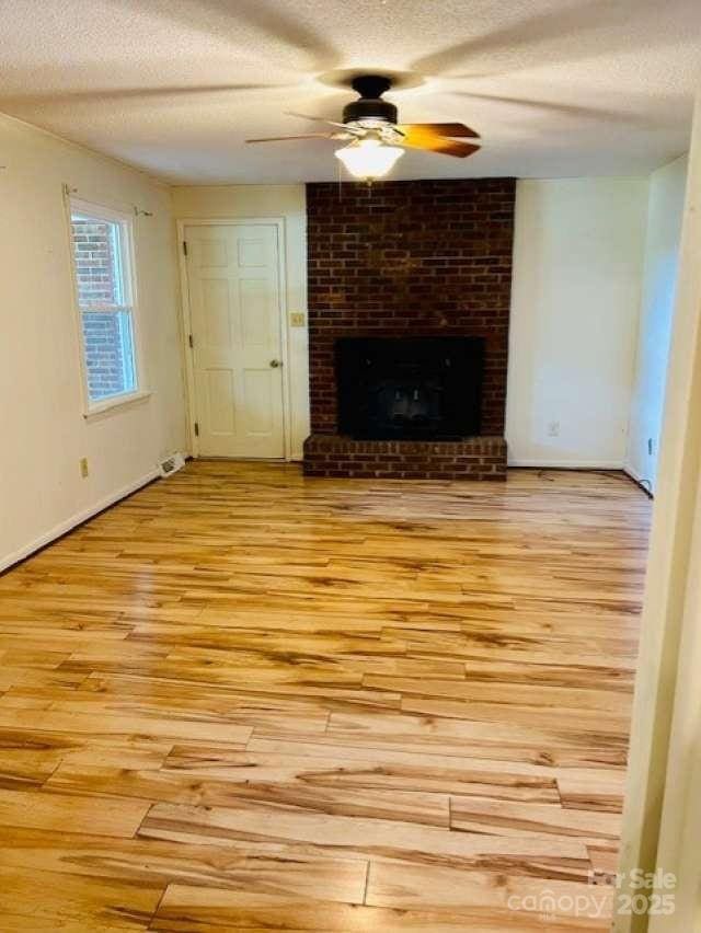2660 Tiffany St, Conover, NC 28613 - unfurnished living room with light wood-style flooring, ceiling fan, a textured ceiling, and a brick fireplace