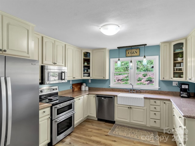 463 Golf Course Rd, Clyde, NC 28721 - kitchen featuring appliances with stainless steel finishes, cream cabinets, light wood finished floors, and glass insert cabinets