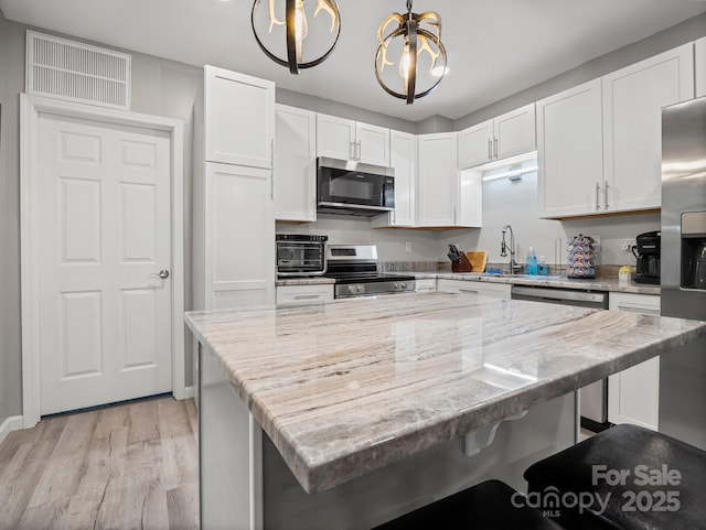 714 Bolt Rd, Lake Lure, NC 28746 - kitchen with stainless steel appliances, white cabinetry, light wood-type flooring, a kitchen breakfast bar, and a kitchen island
