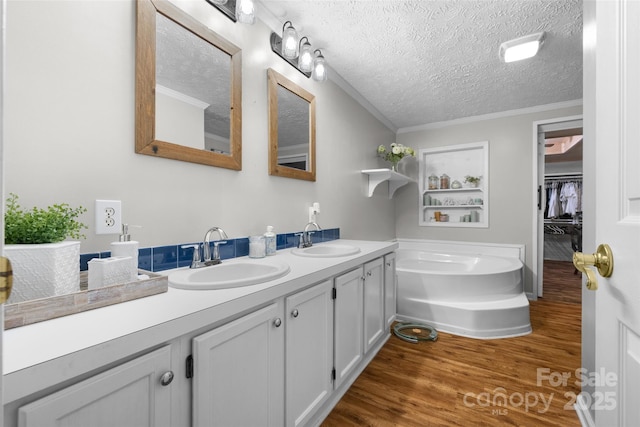 4534 Pebblebrook Cir SW, Concord, NC 28027 - bathroom featuring double vanity, a bath, a textured ceiling, wood finished floors, and ornamental molding