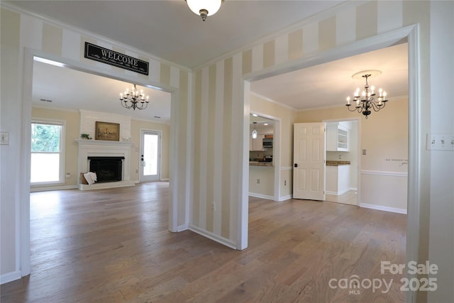8829 Gelligum Dr, Charlotte, NC 28277 - unfurnished living room featuring a chandelier, crown molding, wood finished floors, a large fireplace, and wallpapered walls