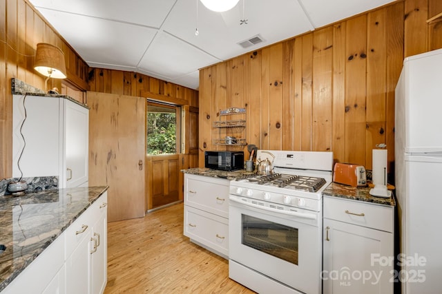203 Laurel Ln, Little Switzerland, NC 28752 - kitchen with white appliances, wooden walls, light wood finished floors, dark stone counters, and white cabinets