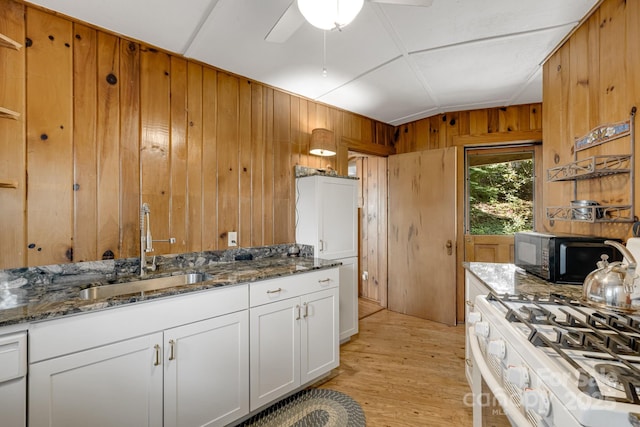 203 Laurel Ln, Little Switzerland, NC 28752 - kitchen with wooden walls, ceiling fan, dark stone countertops, light wood-style flooring, and white cabinets