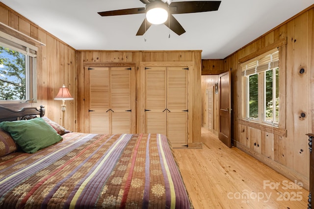 203 Laurel Ln, Little Switzerland, NC 28752 - bedroom featuring wood walls, multiple windows, light wood finished floors, two closets, and a ceiling fan