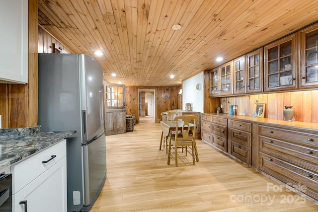 203 Laurel Ln, Little Switzerland, NC 28752 - kitchen featuring freestanding refrigerator, wood walls, light wood-style floors, glass insert cabinets, and dark stone counters