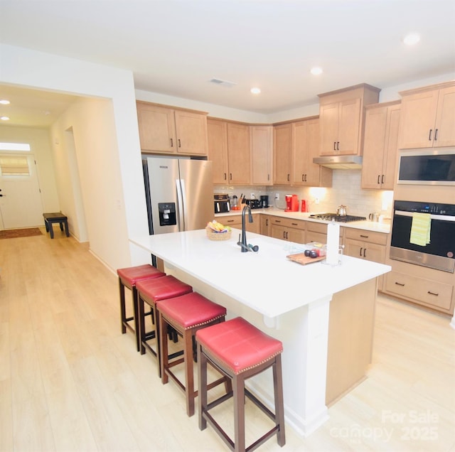 12209 Riceland Way, Midland, NC 28107 - kitchen with stainless steel appliances, under cabinet range hood, light brown cabinets, a breakfast bar, and recessed lighting