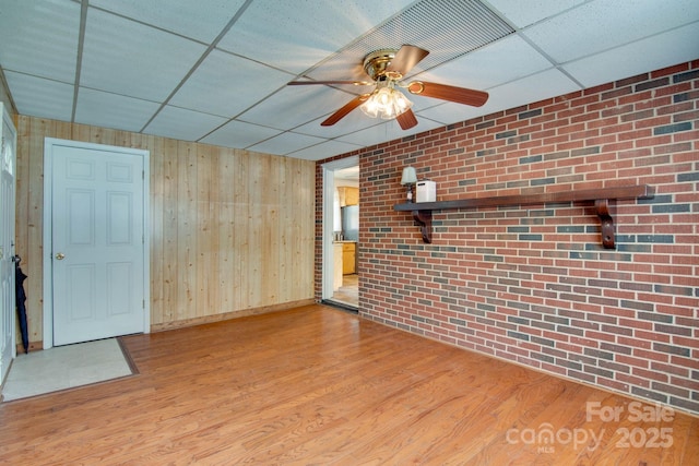 2310 Honeysuckle Pl, Lenoir, NC 28645 - unfurnished living room featuring a drop ceiling, ceiling fan, wooden walls, wood finished floors, and brick wall