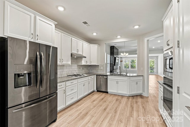 7315 Surprise Ct, Charlotte, NC 28215 - kitchen with stainless steel appliances, under cabinet range hood, a chandelier, light wood-style flooring, and white cabinets