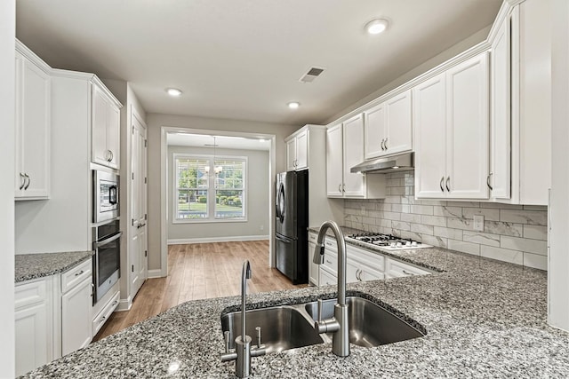 7315 Surprise Ct, Charlotte, NC 28215 - kitchen featuring appliances with stainless steel finishes, under cabinet range hood, wood finished floors, white cabinetry, and dark stone counters