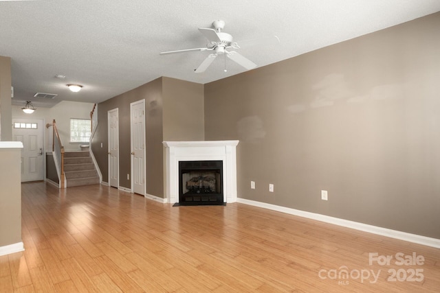 10613 Prairie Ridge Ln, Charlotte, NC 28213 - unfurnished living room with a ceiling fan, stairs, light wood finished floors, a fireplace with flush hearth, and a textured ceiling