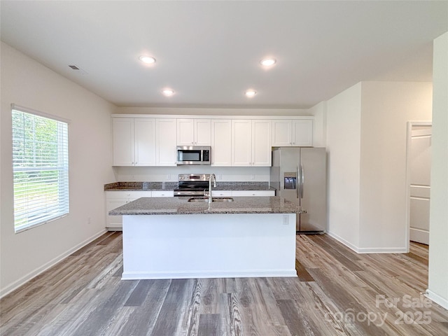1542 Antioch Dr, Conover, NC 28613 - kitchen with stainless steel appliances, a kitchen island with sink, dark stone countertops, white cabinetry, and light wood-type flooring