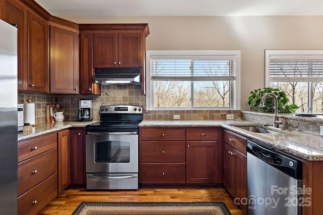 244 Timberlake Rd, Bostic, NC 28018 - kitchen with appliances with stainless steel finishes, under cabinet range hood, light wood-style flooring, light stone counters, and tasteful backsplash