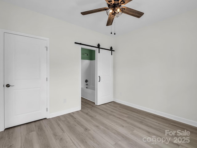 174 Charlie Randall Rd, Lawndale, NC 28090 - unfurnished bedroom with a barn door, light wood-style flooring, ensuite bathroom, and ceiling fan