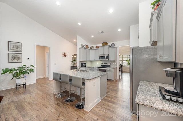 7718 Village Pkwy, Locust, NC 28097 - kitchen featuring appliances with stainless steel finishes, lofted ceiling, gray cabinetry, a kitchen bar, and decorative backsplash