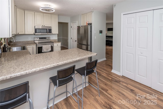 2085 Chapel Creek Rd SW, Concord, NC 28025 - kitchen with appliances with stainless steel finishes, a peninsula, dark wood finished floors, a breakfast bar, and a textured ceiling