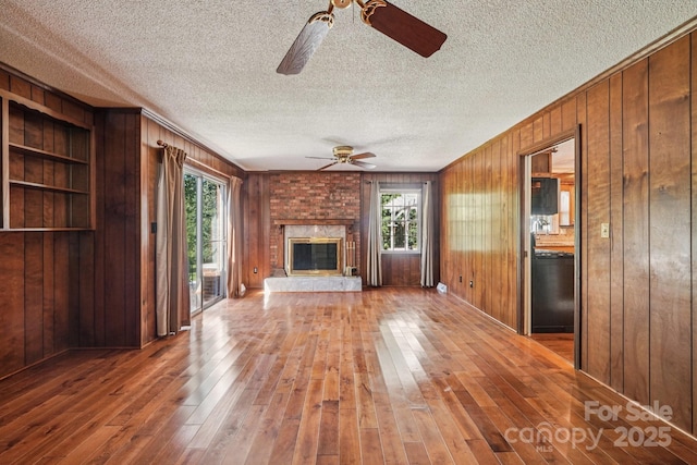 3333 Tanglewood Dr, Rock Hill, SC 29732 - unfurnished living room featuring a ceiling fan, wood walls, hardwood / wood-style flooring, a textured ceiling, and a brick fireplace