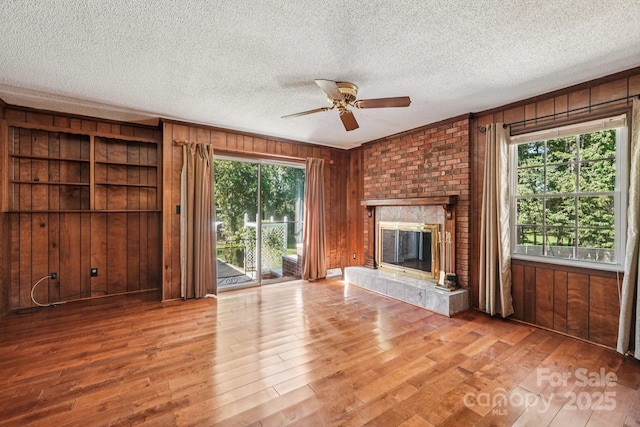 3333 Tanglewood Dr, Rock Hill, SC 29732 - unfurnished living room featuring wood walls, ceiling fan, wood finished floors, a brick fireplace, and a textured ceiling