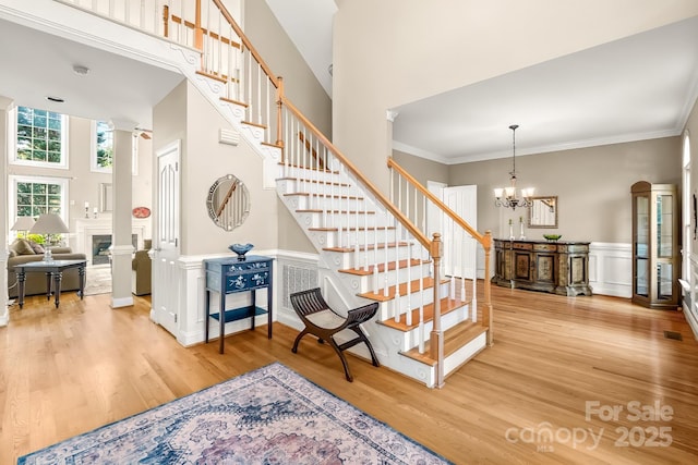 6123 Abergele Ln, Matthews, NC 28104 - stairway featuring decorative columns, wood finished floors, a towering ceiling, a chandelier, and a wainscoted wall