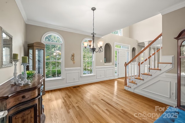 6123 Abergele Ln, Matthews, NC 28104 - foyer with a chandelier, light wood-style floors, stairway, a wainscoted wall, and a decorative wall
