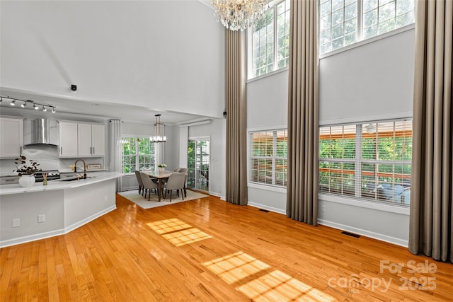12336 Tantallon Ct, Pineville, NC 28134 - kitchen with wall chimney range hood, a chandelier, light countertops, a high ceiling, and light wood-style floors