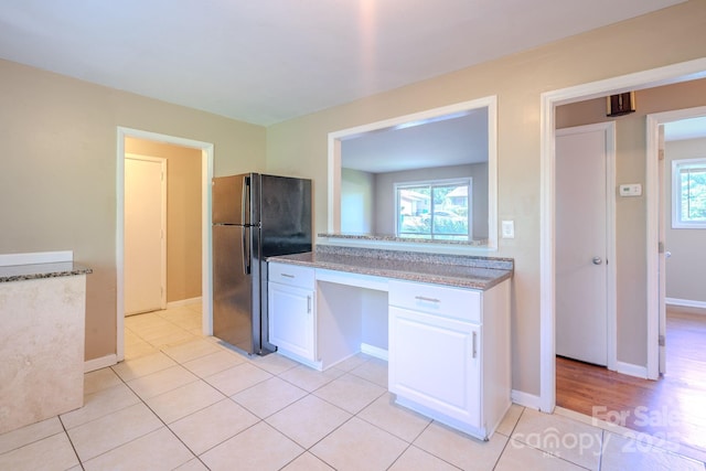 2519 Abelwood Rd, Charlotte, NC 28216 - kitchen with freestanding refrigerator, white cabinets, built in desk, light tile patterned flooring, and stone counters