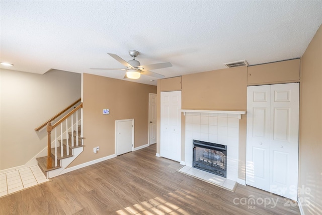 1533 20th Ave NE, Hickory, NC 28601 - unfurnished living room with wood finished floors, ceiling fan, stairway, a tile fireplace, and a textured ceiling