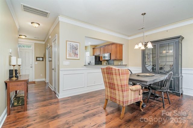 13714 Morehouse St, Huntersville, NC 28078 - dining room featuring crown molding, dark wood-type flooring, a wainscoted wall, a chandelier, and a decorative wall