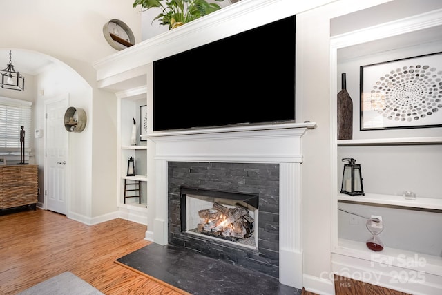 4937 S Hill View Dr, Charlotte, NC 28210 - living area featuring wood finished floors, built in shelves, a lit fireplace, arched walkways, and crown molding