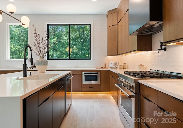 1727 Seifert Cir, Charlotte, NC 28205 - kitchen with stainless steel appliances, wall chimney range hood, light countertops, light wood finished floors, and decorative backsplash