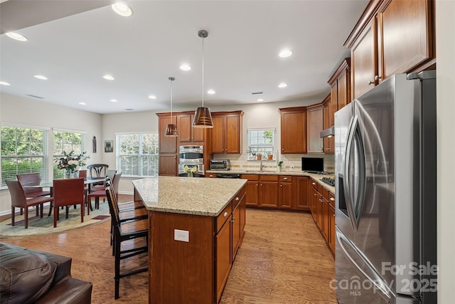 16833 Rudence Ct, Charlotte, NC 28278 - kitchen with appliances with stainless steel finishes, brown cabinets, tasteful backsplash, a kitchen island, and light stone counters