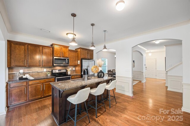 9706 Thyme Ct, Charlotte, NC 28214 - kitchen with appliances with stainless steel finishes, arched walkways, a kitchen breakfast bar, a kitchen island with sink, and brown cabinetry