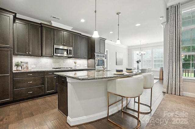 551 Brightleaf Pl NW, Concord, NC 28027 - kitchen with appliances with stainless steel finishes, a kitchen island with sink, light stone countertops, backsplash, and a kitchen breakfast bar