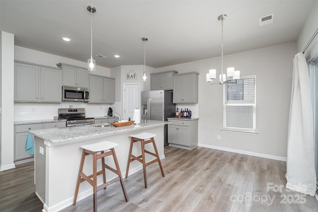 2014 Karen Woods Ln, Charlotte, NC 28216 - kitchen with gray cabinetry, stainless steel appliances, light wood-style flooring, a chandelier, and a kitchen breakfast bar