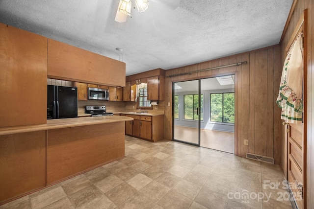 18 Progress Ln, Candler, NC 28715 - kitchen featuring appliances with stainless steel finishes, brown cabinetry, light countertops, wooden walls, and a peninsula