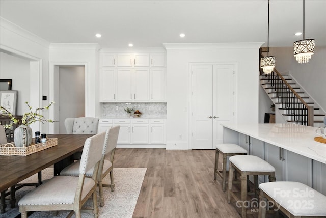 1106 Pomar Cir, Waxhaw, NC 28173 - kitchen featuring light wood finished floors, white cabinets, decorative backsplash, hanging light fixtures, and ornamental molding