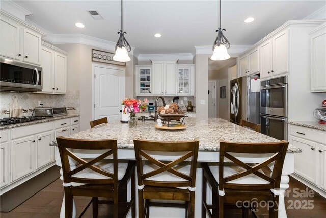 1041 Verbena Ct, Tega Cay, SC 29708 - kitchen featuring appliances with stainless steel finishes, a kitchen breakfast bar, backsplash, an island with sink, and ornamental molding