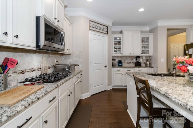 1041 Verbena Ct, Tega Cay, SC 29708 - kitchen with stainless steel microwave, gas stovetop, dark wood-style flooring, white cabinetry, and glass insert cabinets